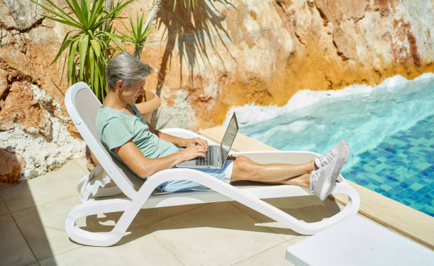 istock Man relaxing by the pool during vacation, typing on keyboard, chatting with friends 1975386583