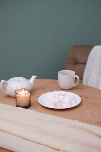 istock Home kitchen interior - white teapot with hot tea, cup of tea, plate with marshmellow, napkin, beige chair on green background. 1975393852