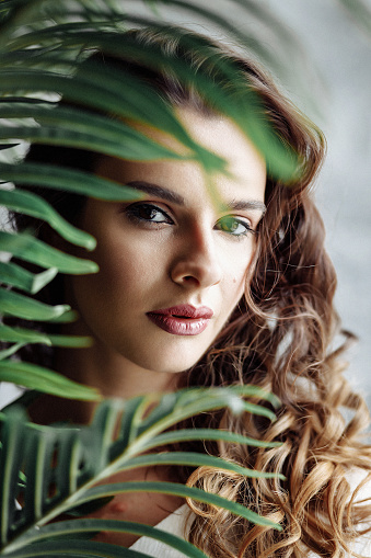 Beautiful woman with perfect skin and natural make-up holding tropical leaves. High quality photo.