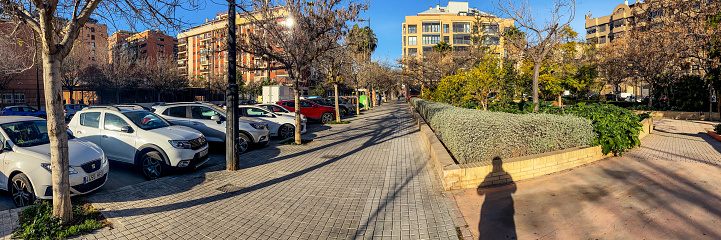 Valencia, Spain - February 3, 2022: Panoramic view of a street in the modern area of the city with a shadow of a man projecting on the sidewalk. Valencia is the capital of the Autonomous Community of the same name and the third biggest city in the country