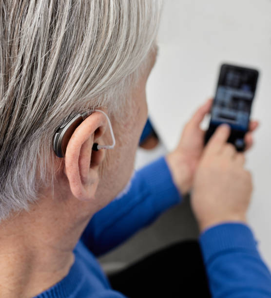 istock Hearing impaired senior man adjusting settings for his BTE hearing aid via smartphone. Hearing aids with innovative technologies at audiology 1975399211