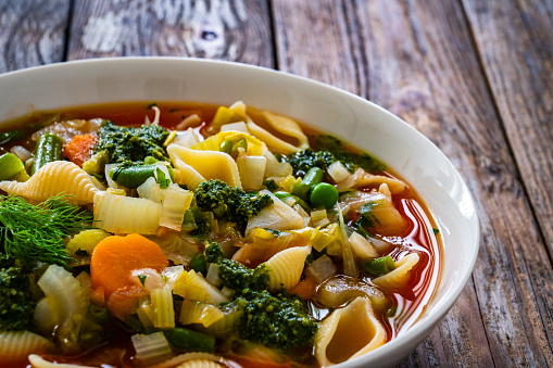 Pistou soup Nice - broth with basil pesto, noodles and vegetables on wooden table in white bowl