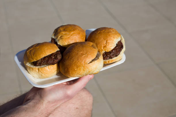Burgers on disposable plates for poor people. Hamburger without anything, bun and cutlet for hungry people in a man's hand