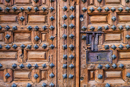 Old wooden door in brown tones with rusty nails and ironwork on the exterior of an old church in the town of Lerma.