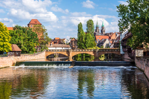 Nuremberg, Germany - August 22, 2023: General view of the Maxbrücke (Max bridge) on the Pegnitz river with the Wasserturm and the Lorenzkirche's towers and in the foreground, the Pegnitzwehr (dam).