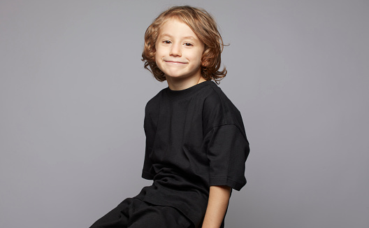 A laughing little boy holds his thumbs up against the white background