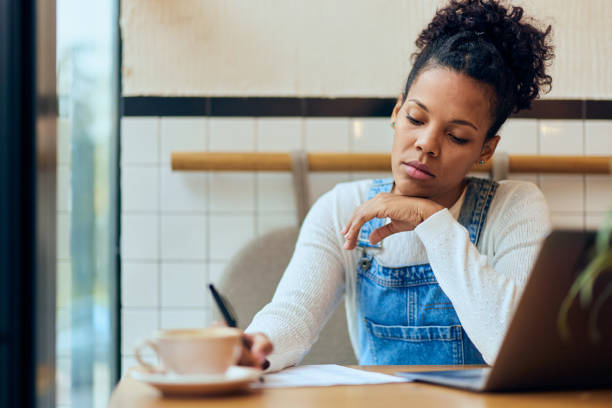 istock A curly-haired smiling African woman writing some notes while sitting at the cafe, working online. 1975470778