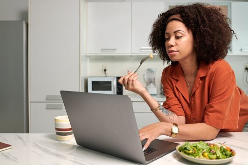Woman leaning on kitchen counter when eating lunch and working on product presentation