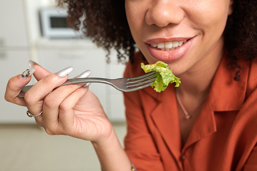 Cropped image of smiling woman eating green salad for lunch