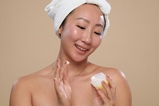 Portrait of smiling young woman with flawless skin applying nourishing cream