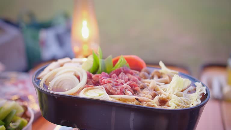 Outdoor hot pot dining experience with fresh vegetables and thinly sliced beef, illuminated by a camping lantern