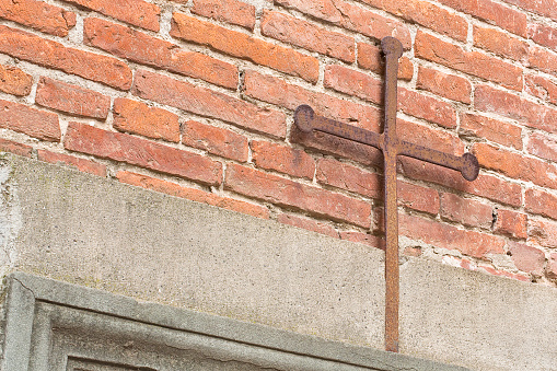 Iron Christian cross snuggled against a brick wall on a italian facade church - image with copy space