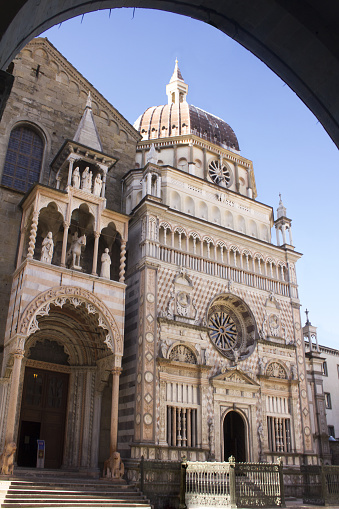 Bergamo Alta, Italy: the facade of the Colleoni Chapel and the portal of the Basilica di Santa Maria Maggiore., seen from under the arch of Palazzo della Ragione. The chapel was built in 1470, but works have continued along the centuries. The Basilica was built from 1133, the Porta dei Leoni Rossi (the portal of the red lions) was designed by Giacomo da Campione in 1353.