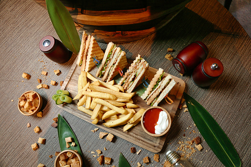 A wooden tray holds a sandwich cut in half and a serving of crispy french fries.