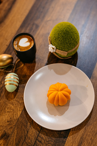 Pumpkin-shaped dessert served with coffee on an Easter-themed table in a café.
