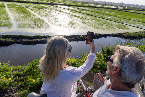 Mature couple pause bicycles in rice paddies and take photos