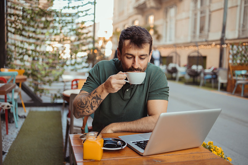 Handsome man enjoying his coffee while working on laptop computer in outside cafeteria