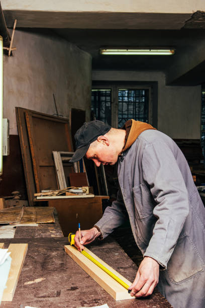 A carpenter works in a workshop with a saw, planer and various tools