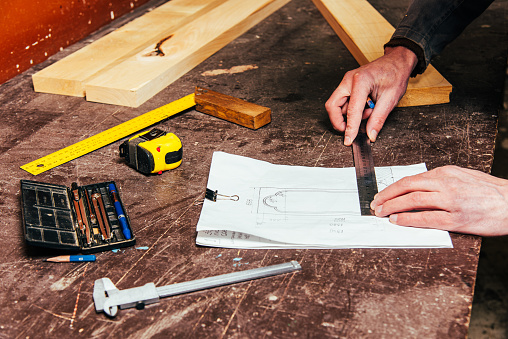 A carpenter works in a workshop with a saw, planer and various tools