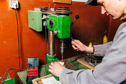 A carpenter works in a workshop with a saw, planer and various tools