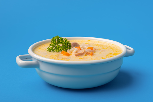 White enamel bowl with delicious chicken soup, greek recipe, with vegetables and lemon juice