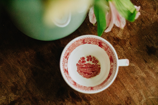 vintage patterned red and white teacup, very decorative on a warm honey wooden tabletop. red rooibos tea, hot tea drink.
