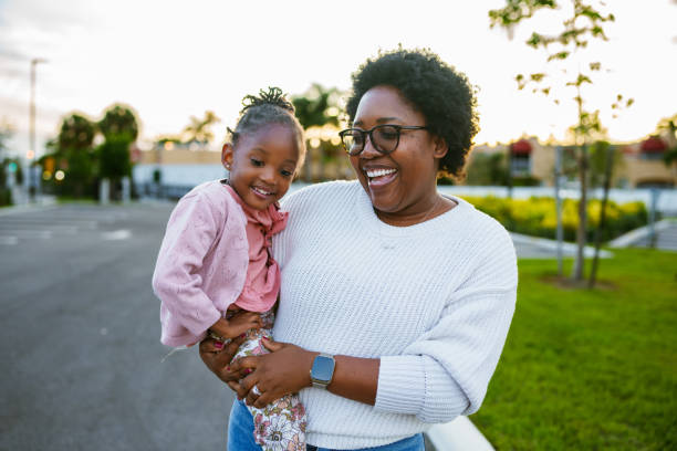 Happy African American mom and daughter on a walk An African American woman carries her three year old daughter on her hip as they take a relaxing and fun walk around their neighborhood in Florida at sunset. black mother and adult daughter stock pictures, royalty-free photos & images