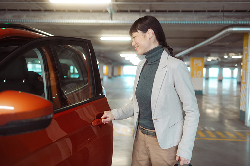Photo of a cheerful Japanese woman opening a car's door
