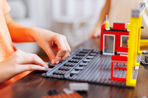 Focused child constructing a colorful building with a toy construction set on a table, showing creativity and concentration.