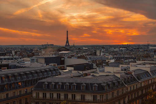 From the rooftop balcony of the renowned shopping center Galeries Lafayette, a breathtaking scene unfolds as the sun sets over Paris. The iconic Opera House and majestic Eiffel Tower stand tall amidst the cityscape, bathed in the warm hues of the evening sky. This enchanting aerial view captures the timeless beauty and romance of the French capital at dusk