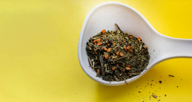 istock Ceramic white spoon with dry tea leaves and various berry additions on a yellow background 1975828578