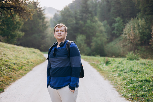 Young male with backpack hiking on the road in nature. 30s men walking on nature in sport clothes.
