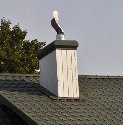 A chimney on the roof of a house covered with metal tiles or a metal profile