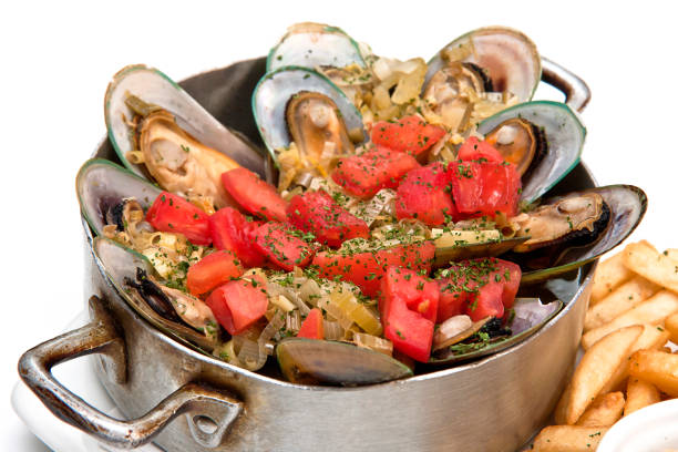 Mussels in a frying pan and on a plate with chips and sauce on white background