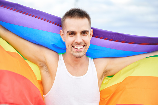 Portrait of a beautiful young gay man with rainbow flag. Fighting for his rights. LGBT concept.