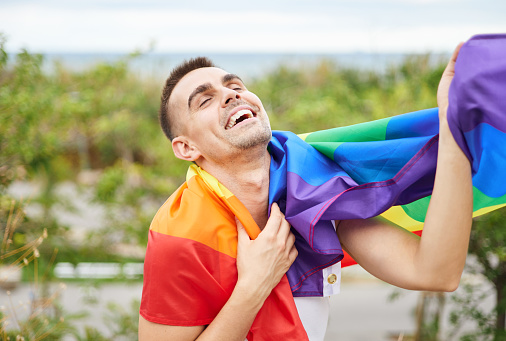 Cheerful young man with a rainbow flag on pride day