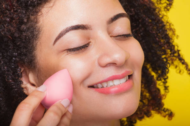 istock Extreme close-up of a woman's face smiling while applying makeup with a sponge 1975925905