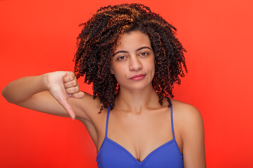 Woman isolated on an orange background with a disapproving expression, giving a thumbs-down