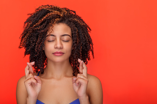 Beautiful Brazilian woman isolated on an orange background with closed eyes and fingers crossed