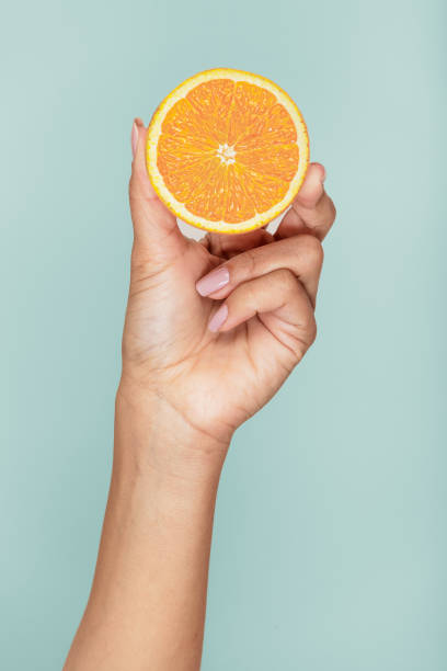 istock female hand holding half an orange on a light blue background 1975930646