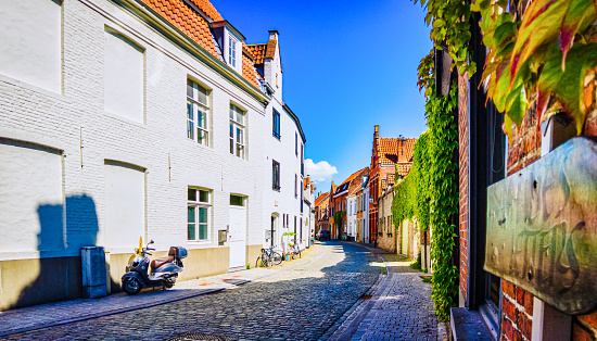 Bicycles, a motorbike and a car are parked along a narrow curved cobblestone street in Bruges. Belgium