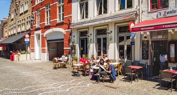 Bruges, Belgium- June 3, 2023- People enjoy early June weather to dine al fresco   in front of old brick buildings in Bruges, Belgium.