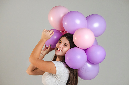 Happy teenage girl with purple and pink balloons in a studio