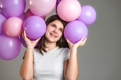 Happy teenage girl with purple and pink balloons in a studio