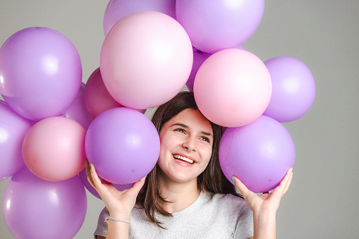 Happy teenage girl with purple and pink balloons in a studio