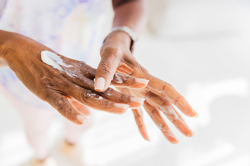 Hands of a mature black woman, applying cream to keep them moisturized