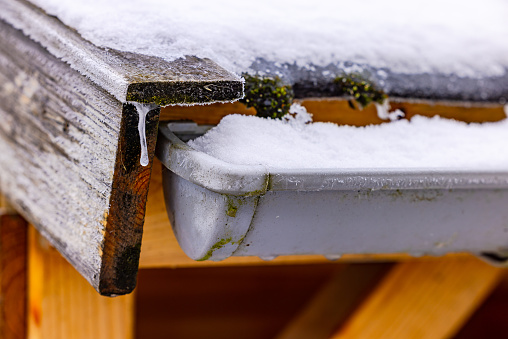 Gutter with snow and wood with icicles on the roof of a wooden hut as a close-up with many details of winter