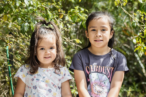 Close up image of two young Maori sisters posing for their photograph to be taken outside in a nature setting.