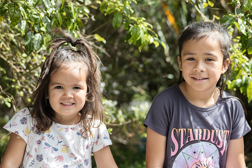 Close up image of two young Maori sisters posing for their photograph to be taken outside in a nature setting.
