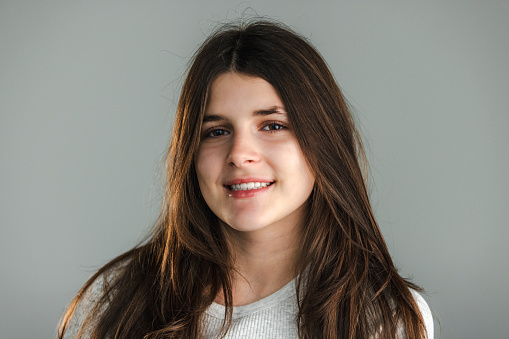 Studio portrait of a teenage girl with long brown hair, wearing a light t-shirt